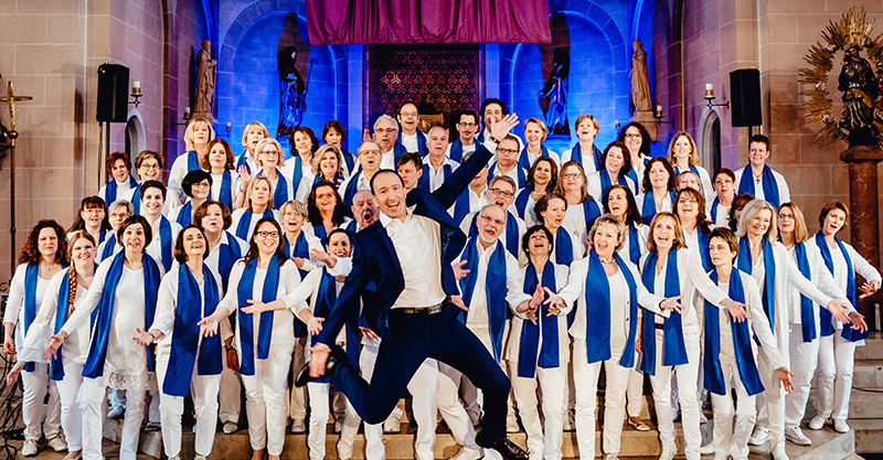 Gospelchor Grenzenlos mit Chorleiter auf der Bühne in einer Kirche